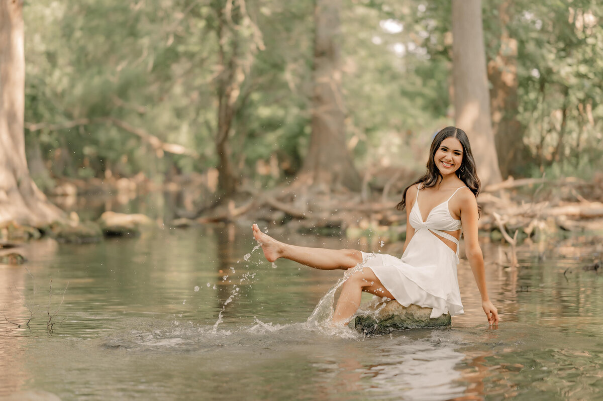 Senior girl splashes in the water at Cibolo Creek Nature Center during senior pictures.