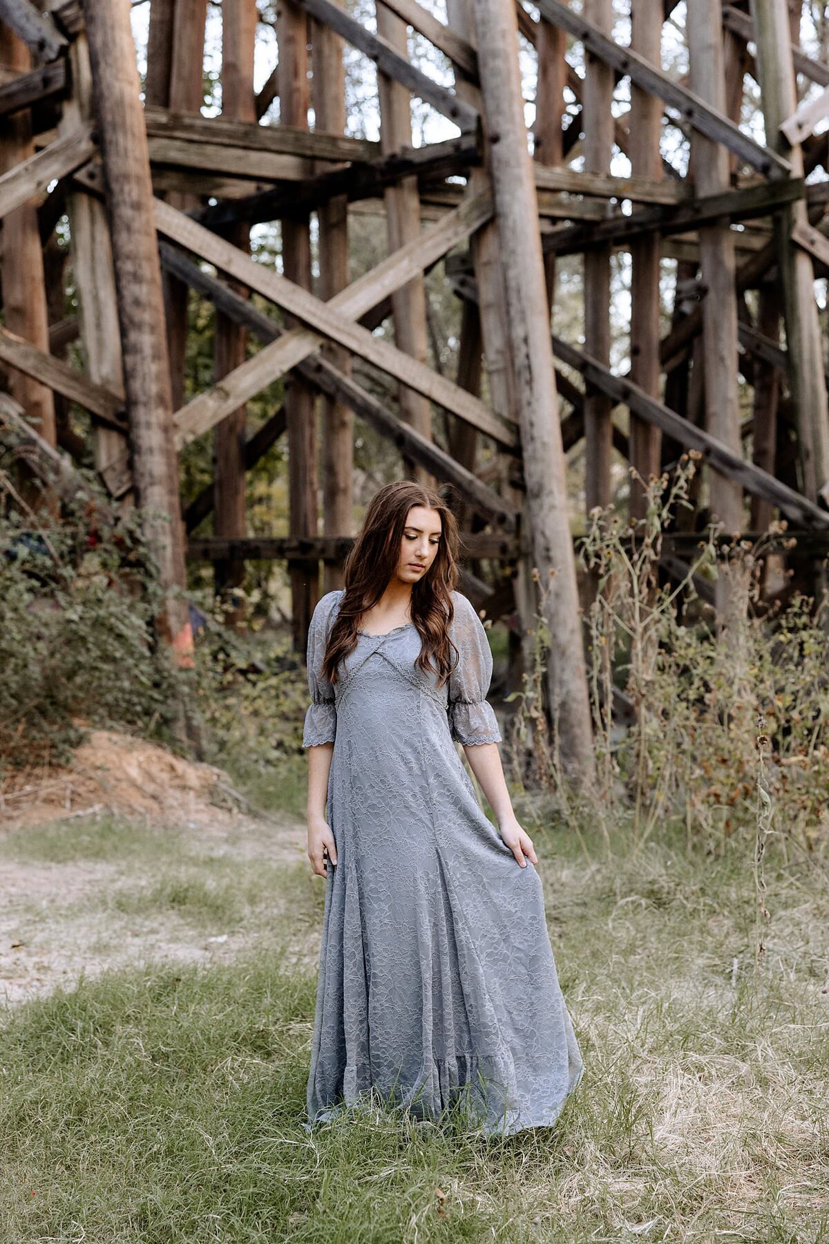 Senior portrait of a young girl dressed in a dusty blue dress in front of an old bridge.