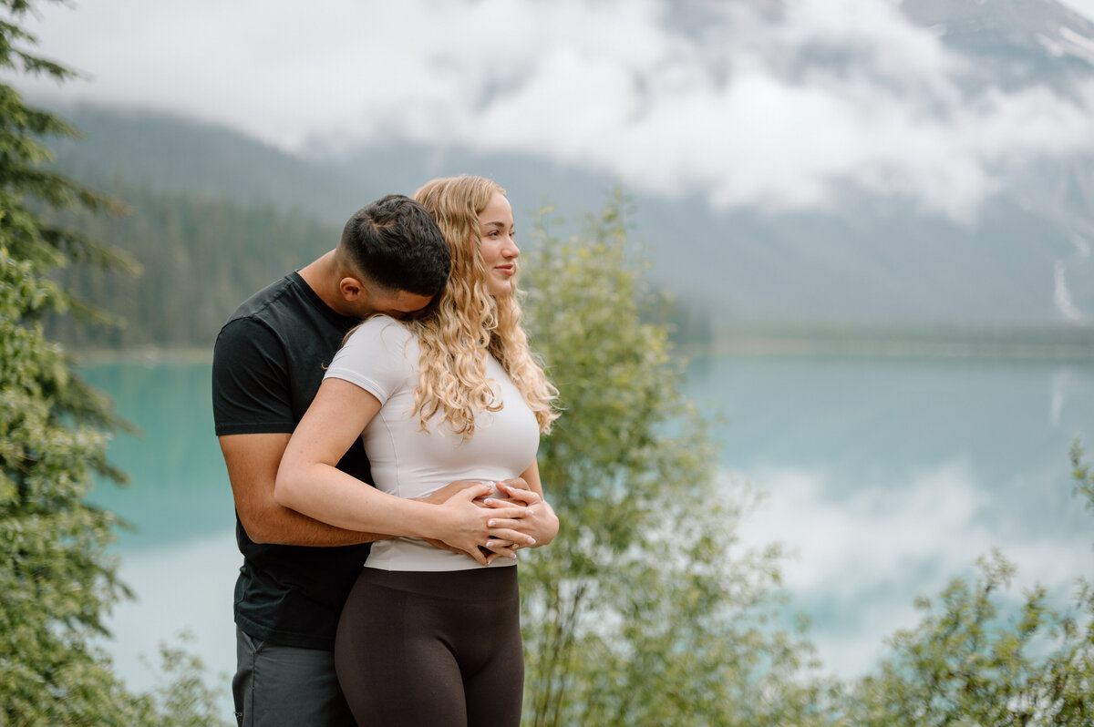 Romantic embrace in the mist at Emerald Lake with vibrant forest and mountain scenery.