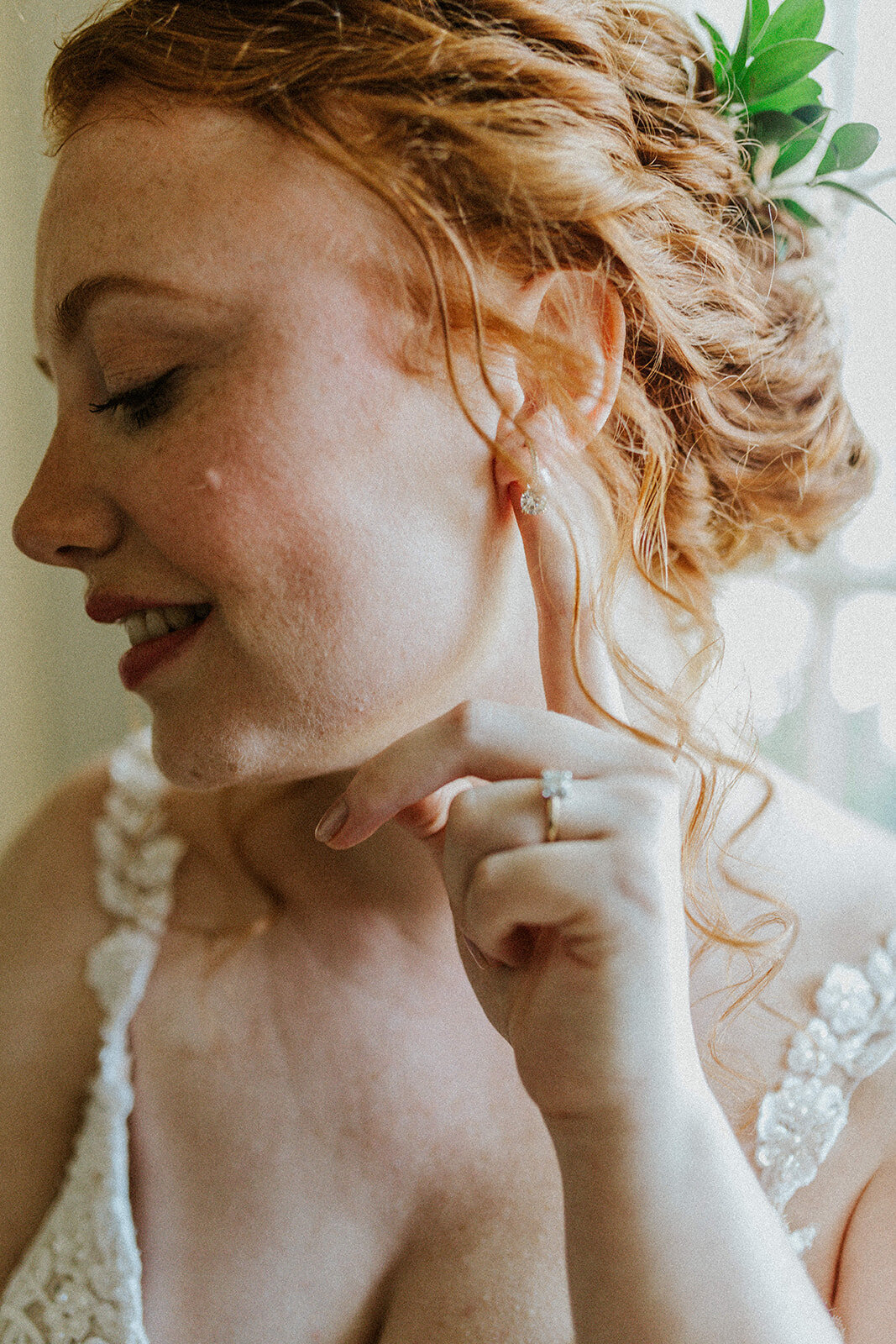A woman in a white lace dress models her dainty earrings on her wedding day