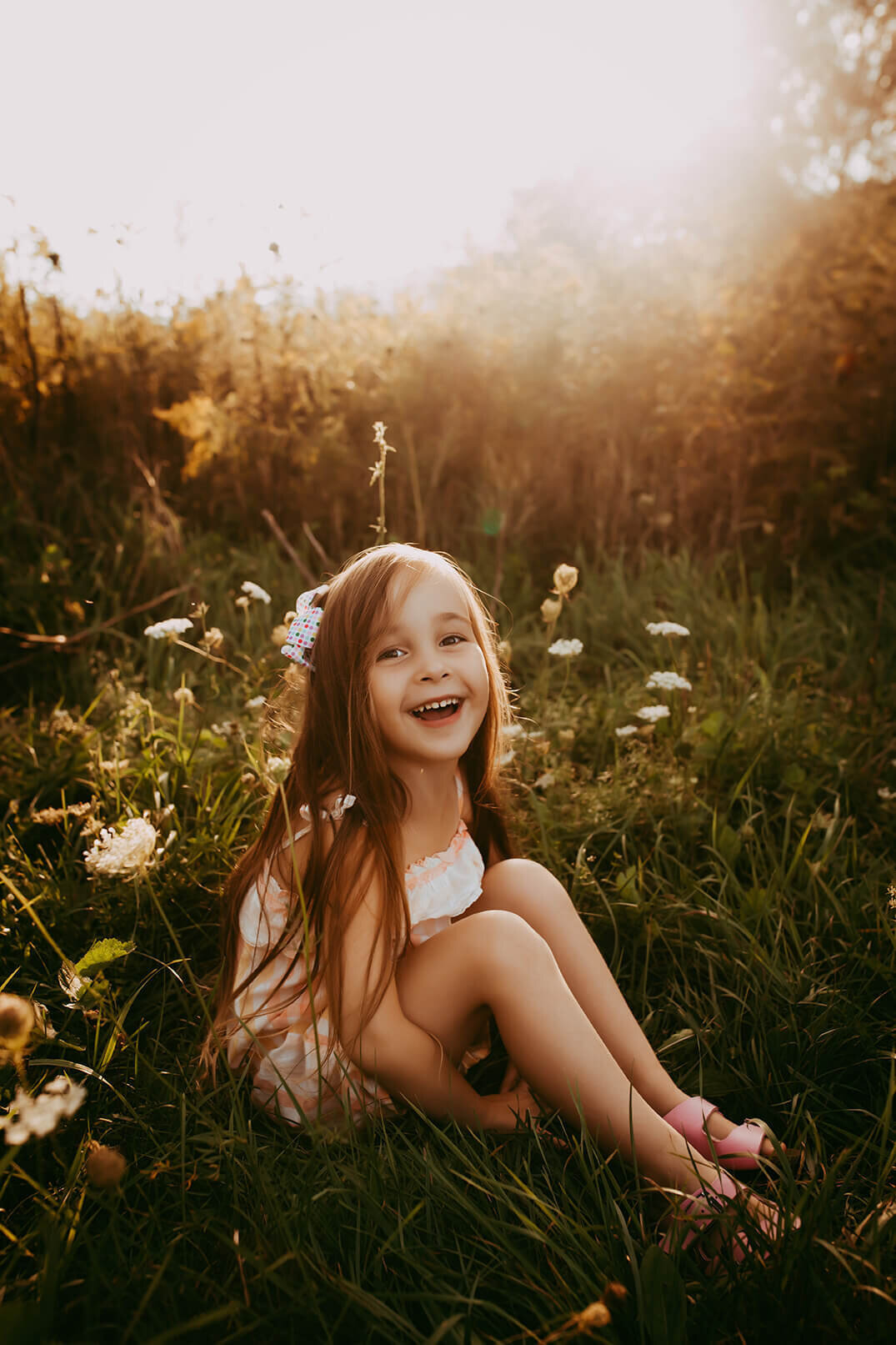 a little girl sitting in an open field holding her legs and smiling at sunset in rochester, ny