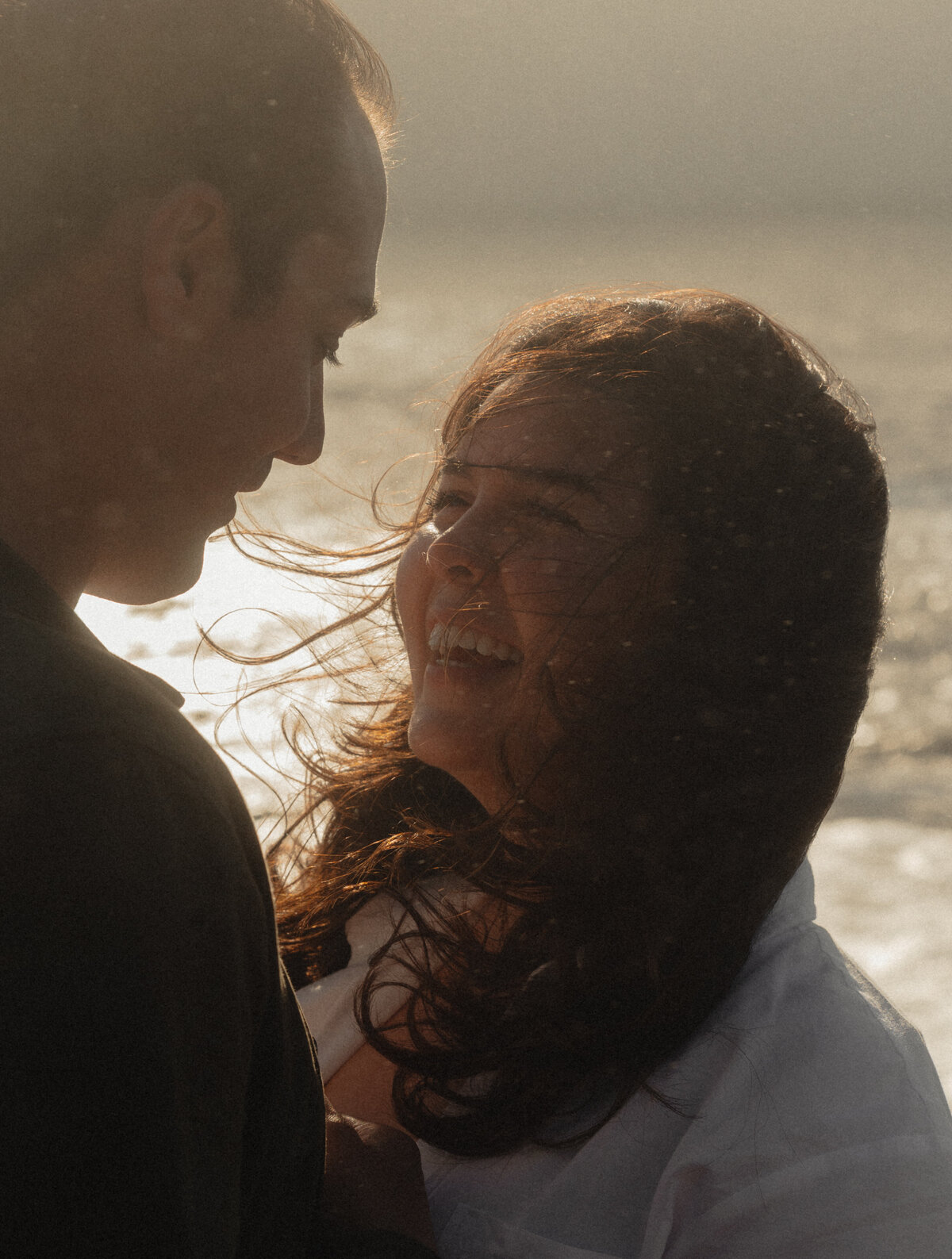 woman smiling at her partner while the wind lifts her hair on a breezy coastal cliff