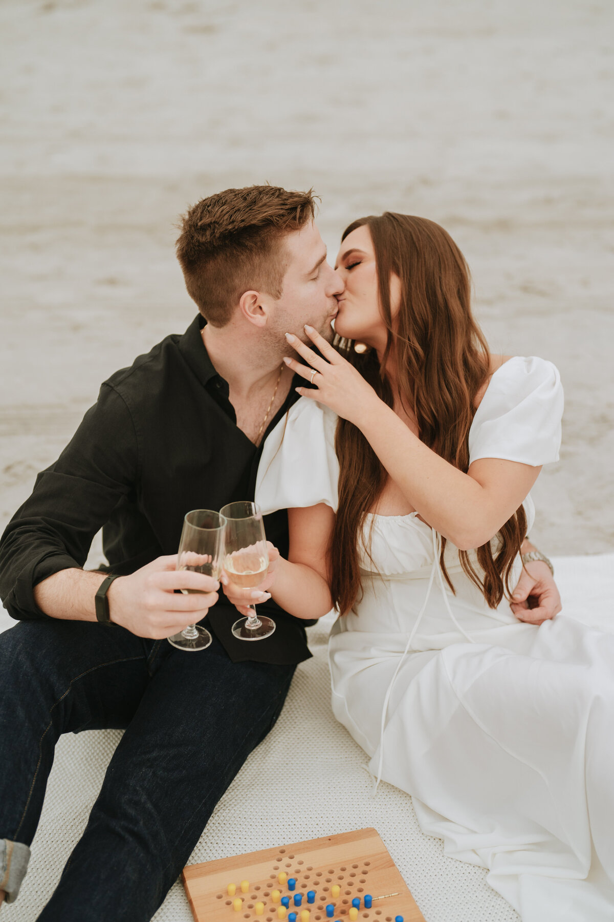 couple playing chinese checkers and doing a champagne cheers on the beach while kissing