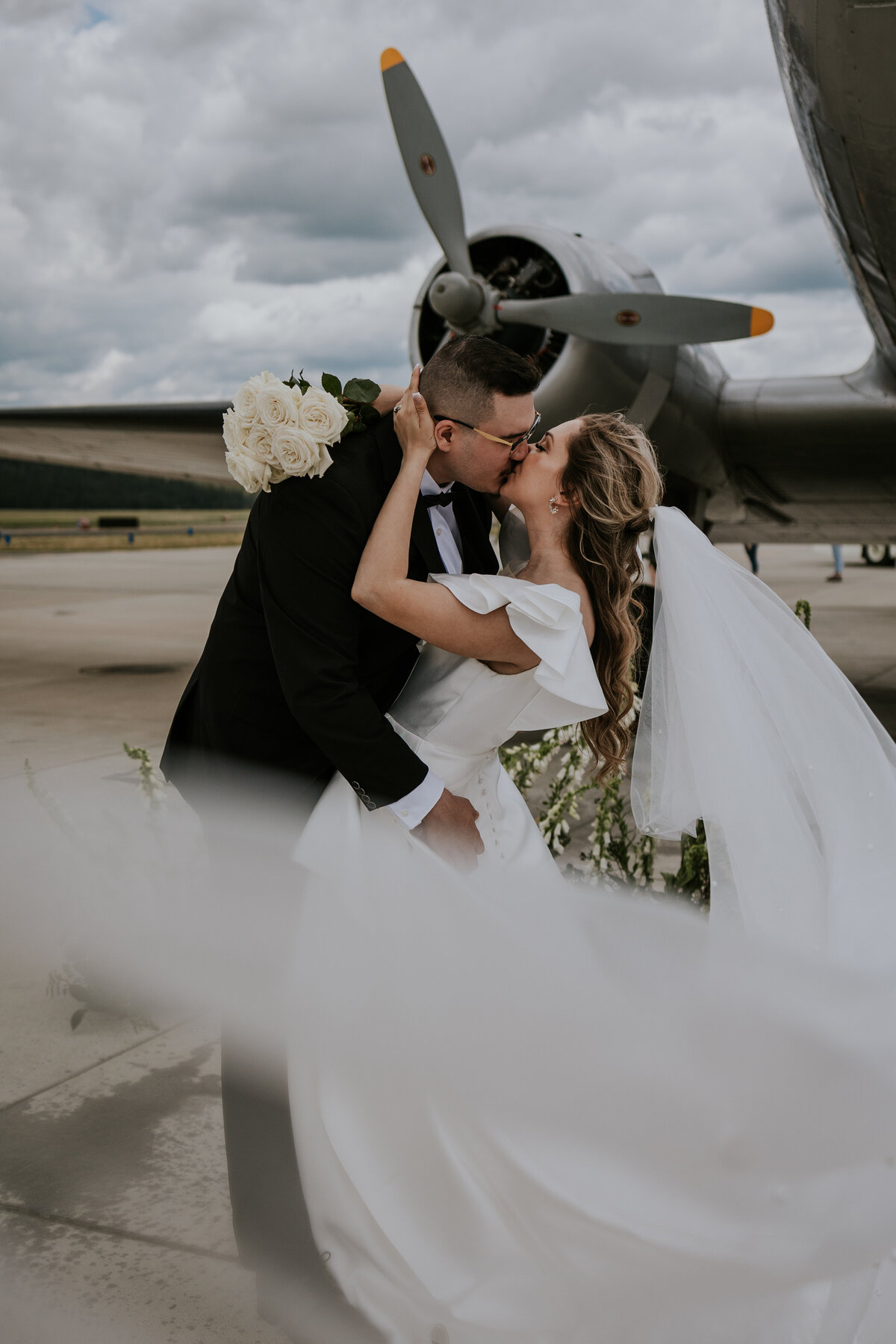 Bride and groom kiss while standing in front of WWII plane.