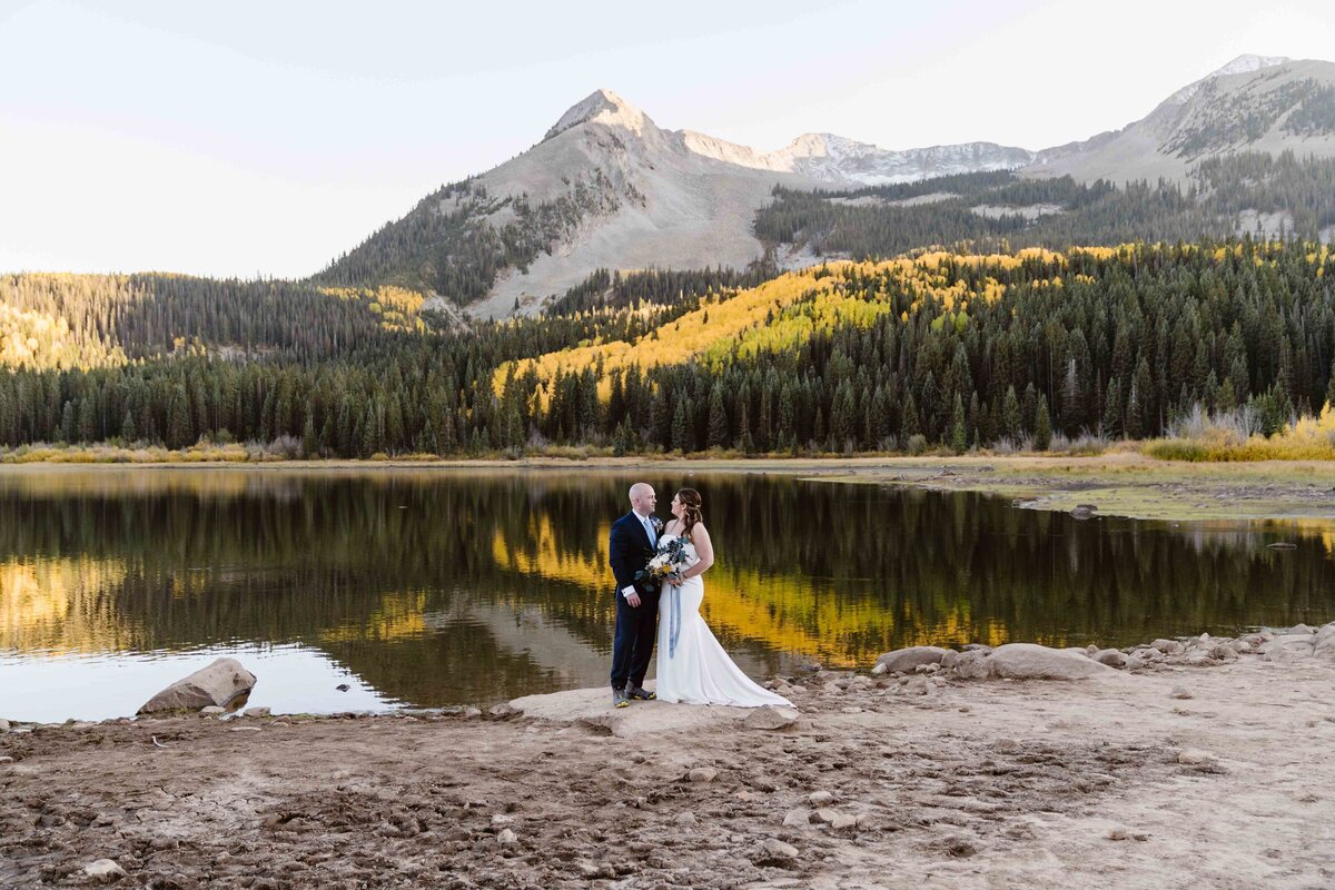 Crested Butte Colorado elopement with couple standing on a rock overlooking an alpine lake in the fall with yellow Aspen trees reflecting in the lake