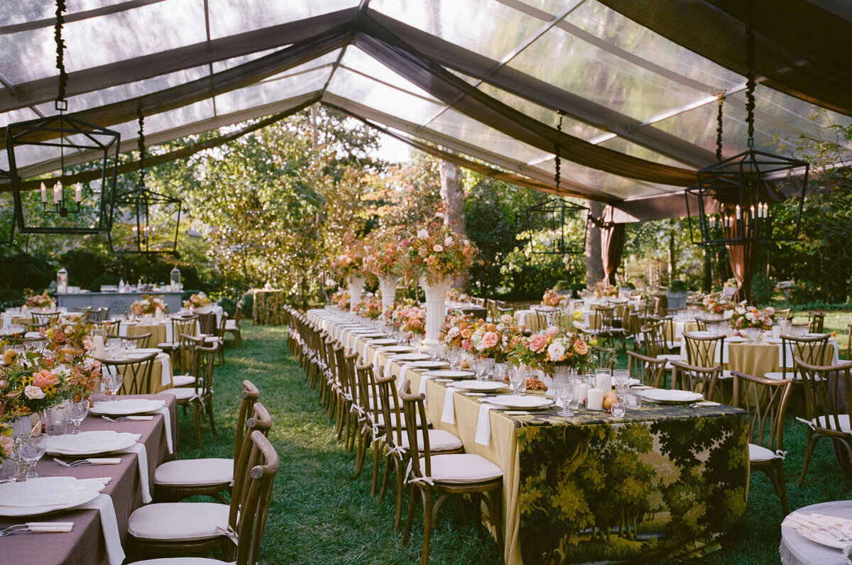 Lush fall florals for low and high centerpieces at fall wedding reception. Clear tented wedding reception in the family's back yard creating an intimate wedding reception environment. Whimsical and organic floral design in colors of copper, yellow, blush,and brown. Fall florals with sweet peas, dahlias, butterfly ranunculus, roses, mums, and bittersweet berries. Design by Rosemary & Finch Floral Design in Nashville, TN.