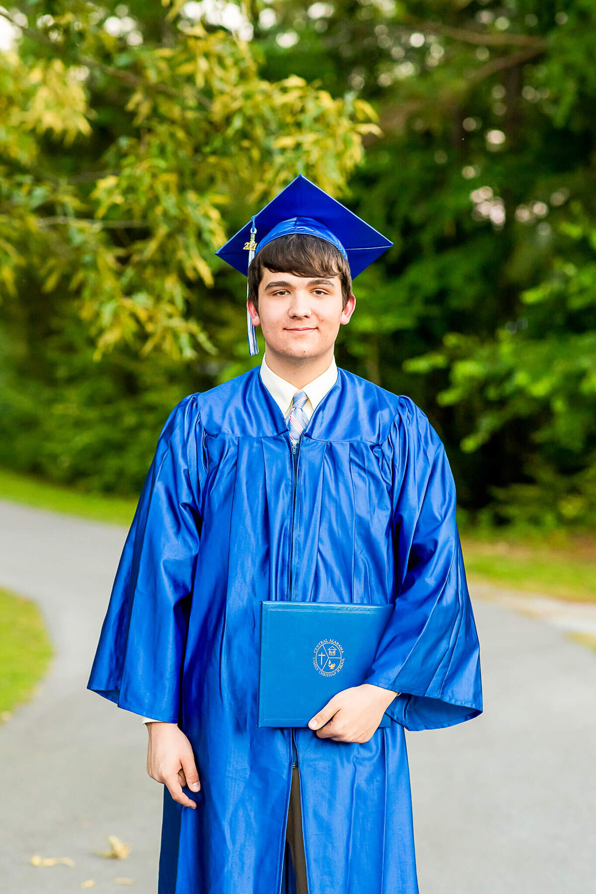 Senior boy in his cap and gown holds his diploma after graduation