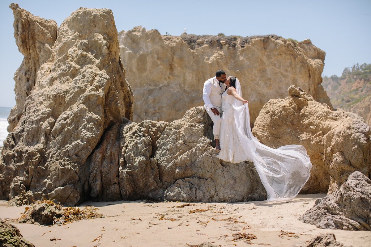 bride and groom embrace on the beach with the ocean in the background