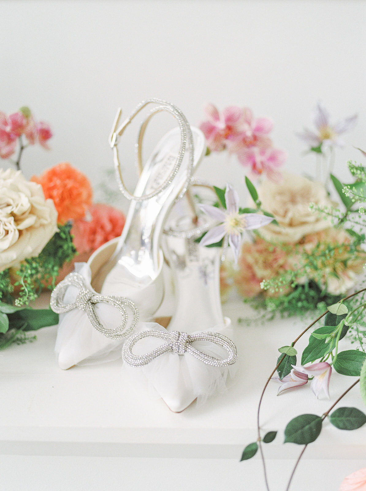 Silver wedding shoes displayed amongst bright, lush, wedding flowers.