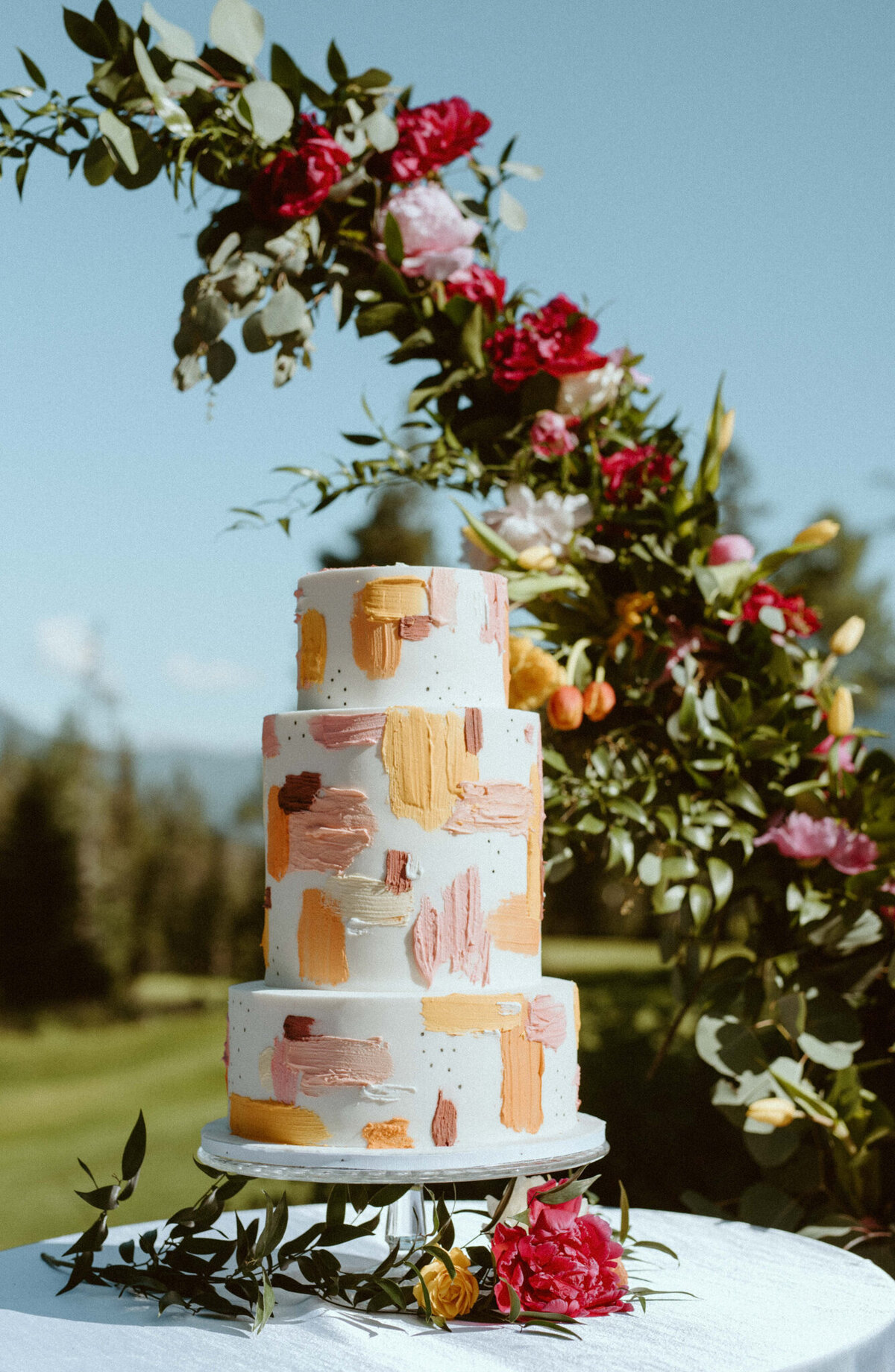 Trendy and unique three-tiered wedding cake with pink and orange buttercream painted details, by Yvonne's Delightful Cakes, classic cakes & desserts in Calgary, Alberta, featured on the Brontë Bride Vendor Guide.