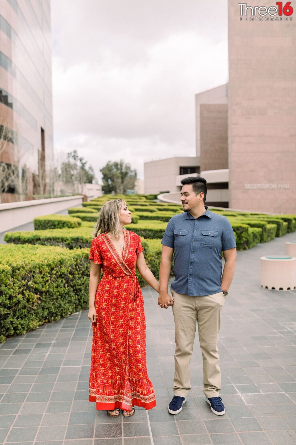 Engaged couple hold hands and look at each other during photo session