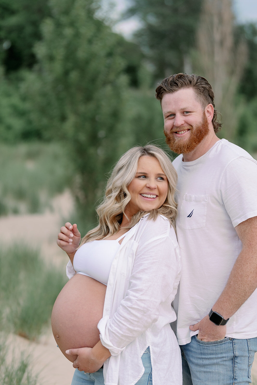 Expecting couple smiling at the camera on the shoreline at South Haven North Beach, Lake Michigan maternity photography.