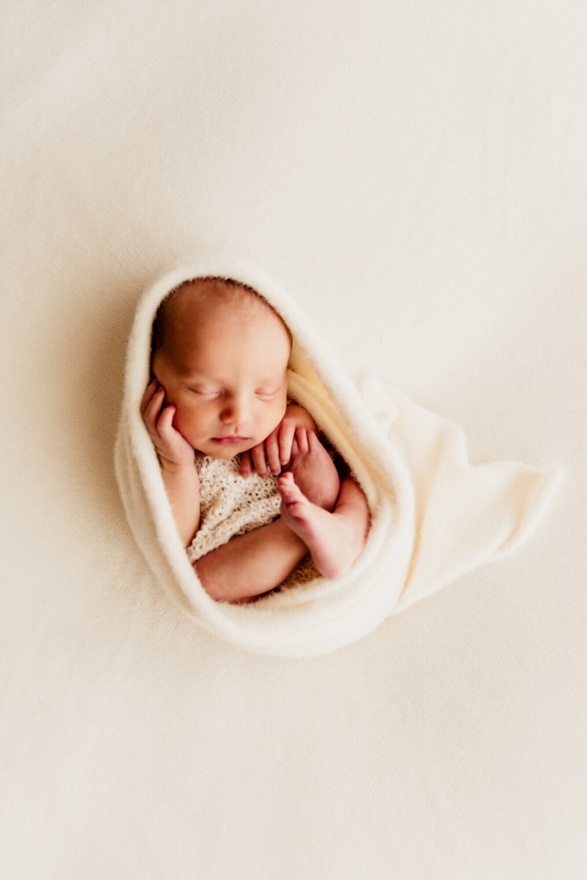 A baby with her hand on her chin and knee swaddled for her newborn photo session, Edmond Oklahoma.