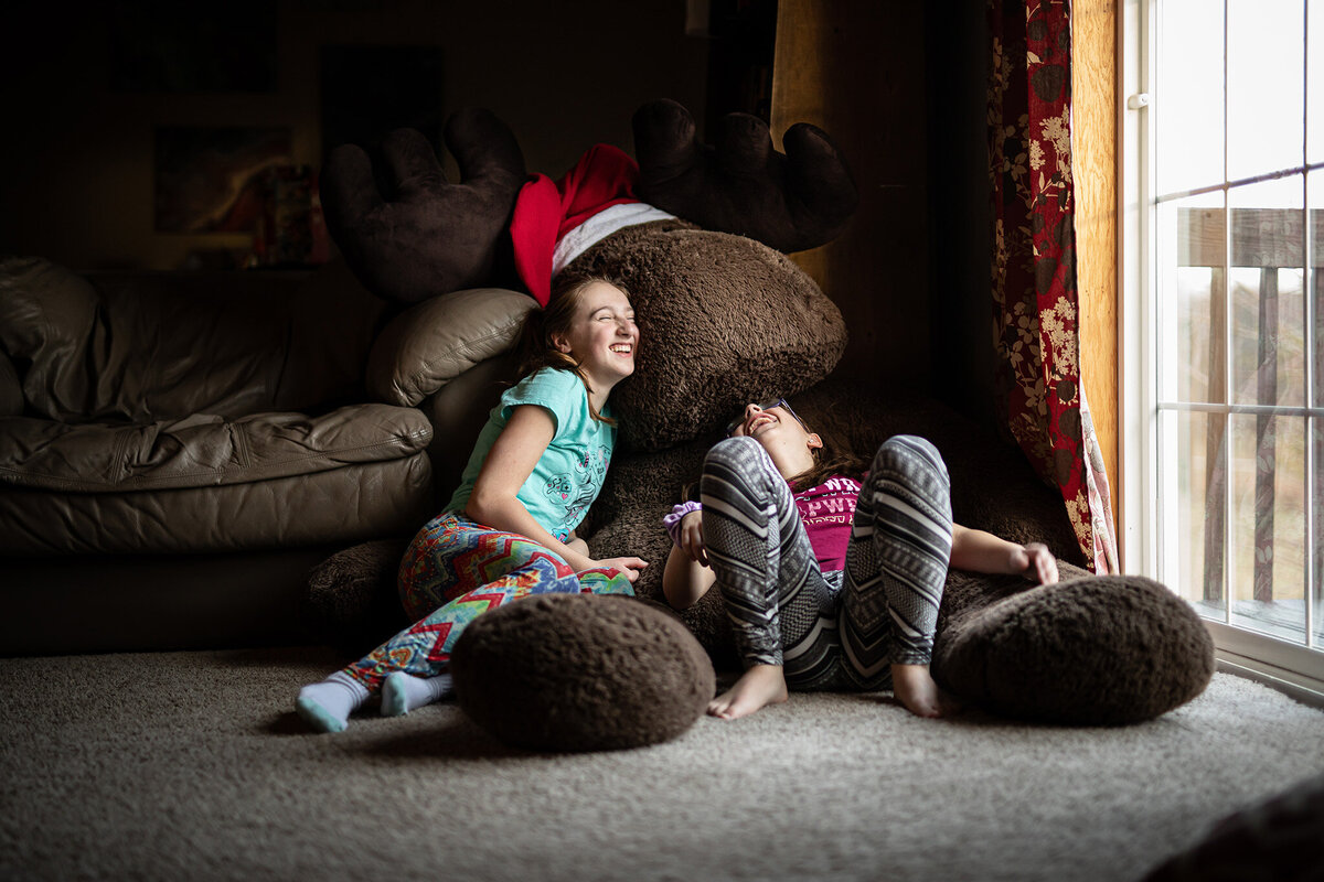 sisters laughing while sitting on giant stuffed christmas moose