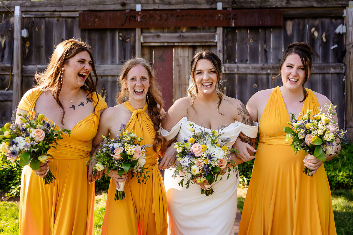 Joyful bridesmaids in sunflower yellow dresses smiling and walking arm and arm with bride