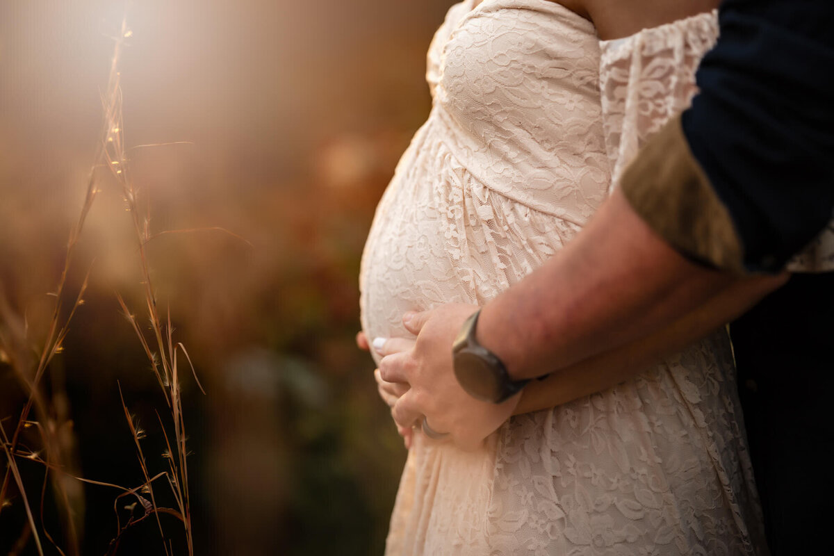 A close up of a baby bump with mom and dads hands cradling