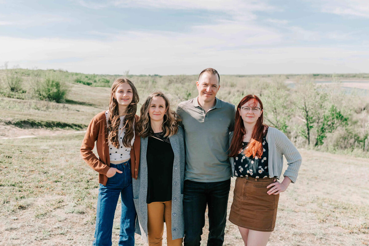 Family of 4 standing side by side on a hill side at cranberry flatts Saskatchewan. 