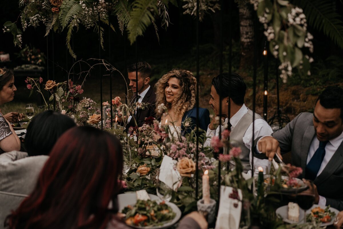 Couple & guests gathered around flower-covered table in the woods during intimate wedding in Olympic National Park!