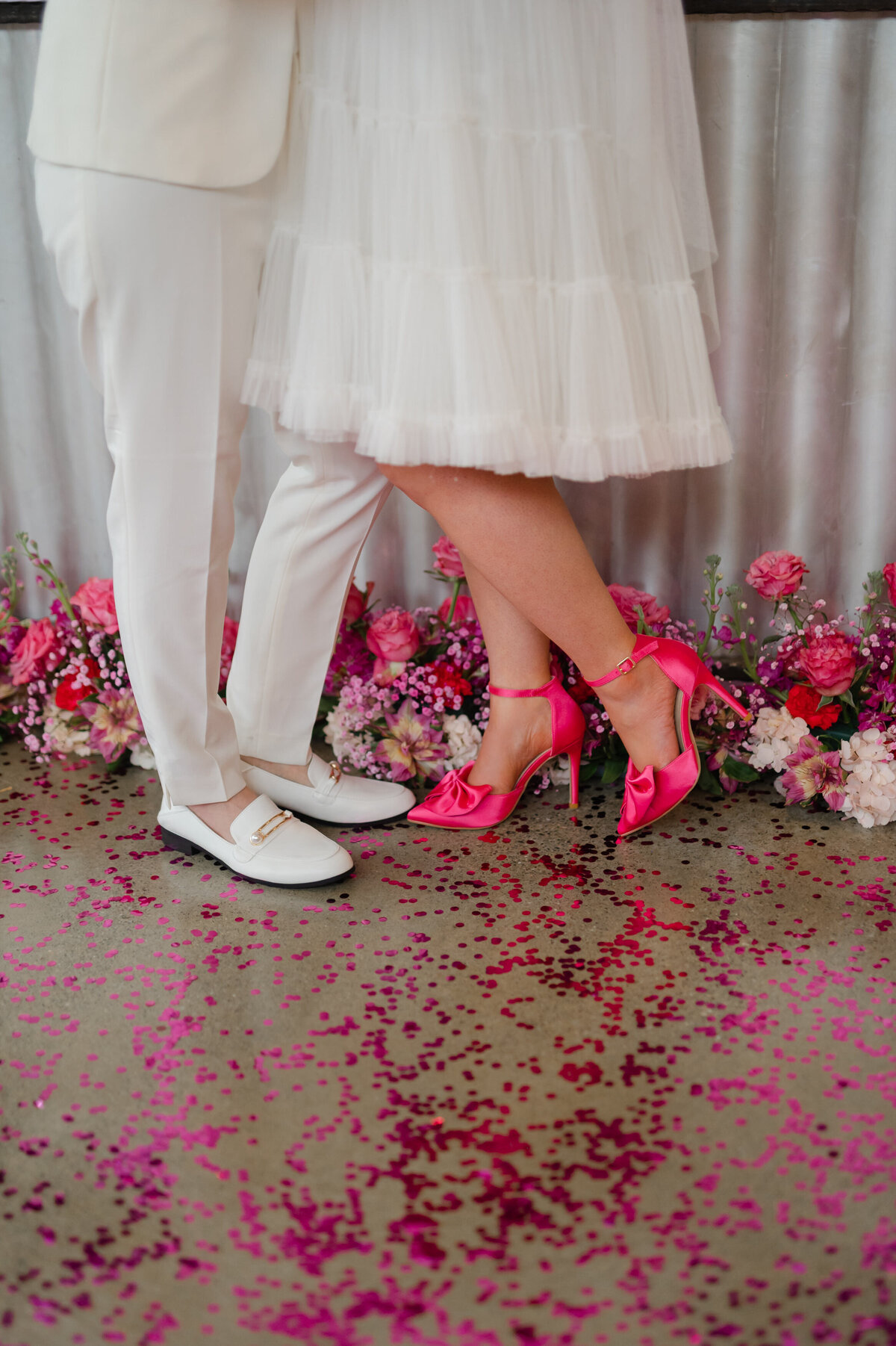 Wedding shoe closeup. The brides are wearing white loafers and hot pink heels.