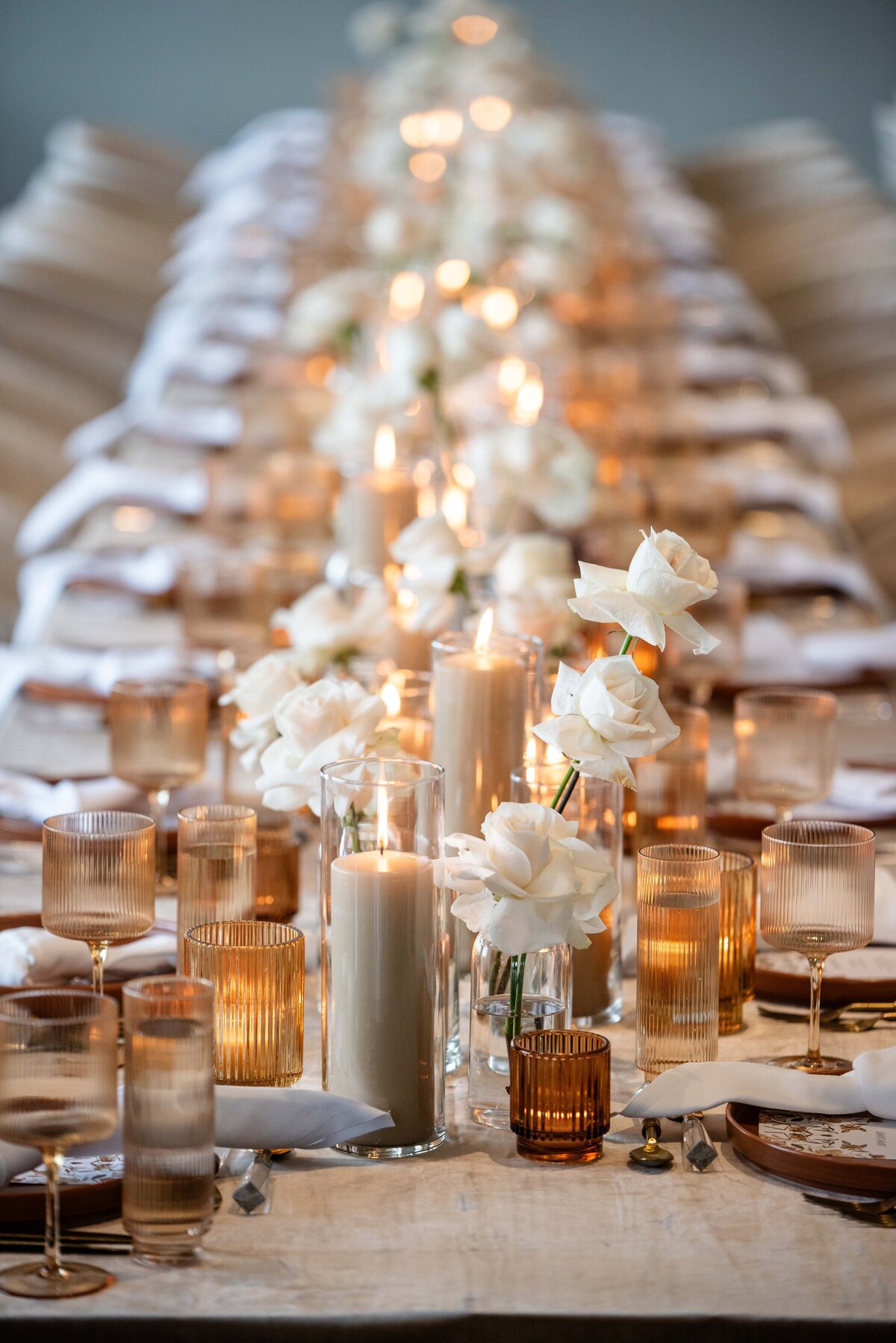 Elegant reception table featuring the Pantone Color of the Year, highlighted through amber and brown votive holders and glass wear, cream pillar candles and  cream roses spanning the length of the table for a sophisticated look