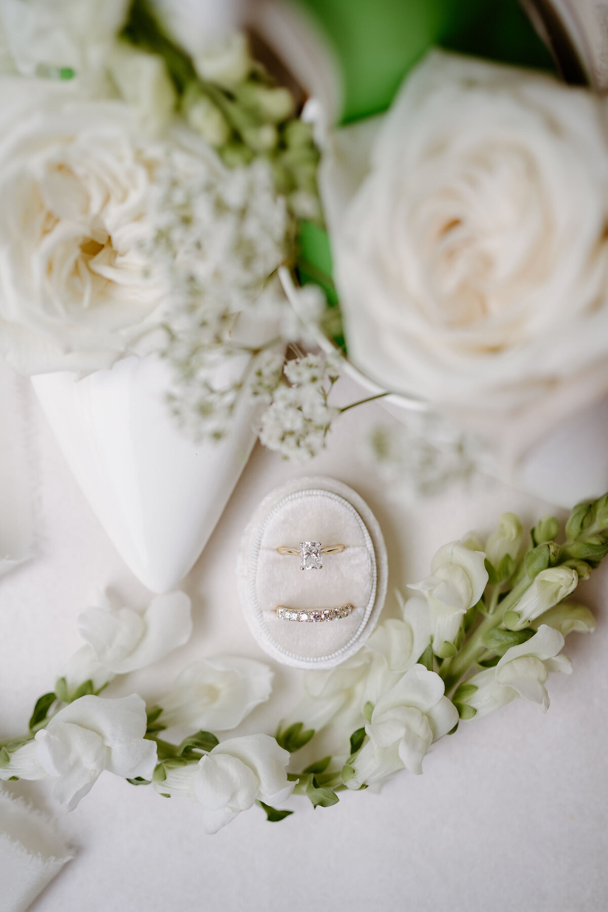 Wedding rings in velvet box surrounded by white florals and romantic wedding details.