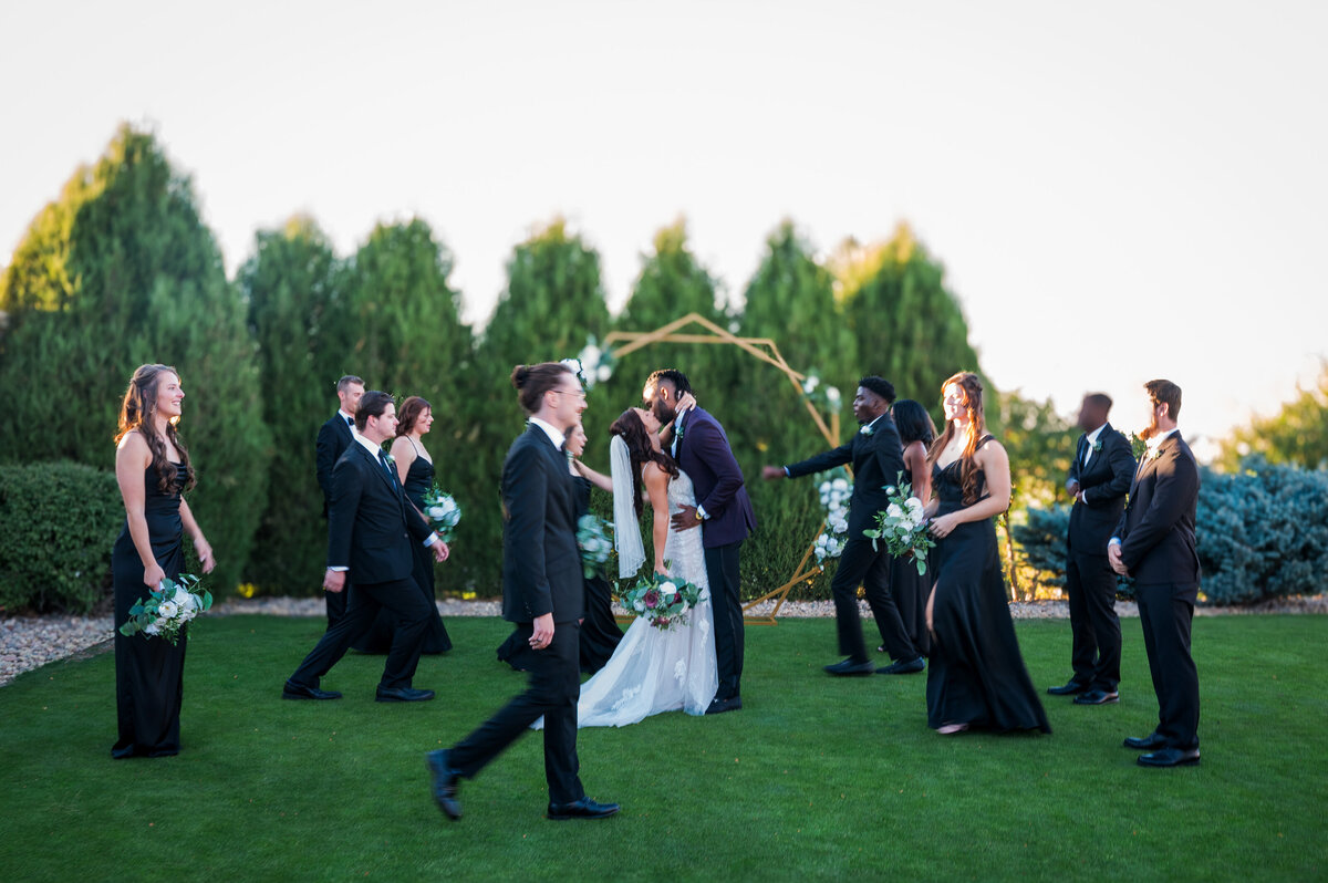A bride and groom share a kiss in the middle while their wedding party walks all around them.