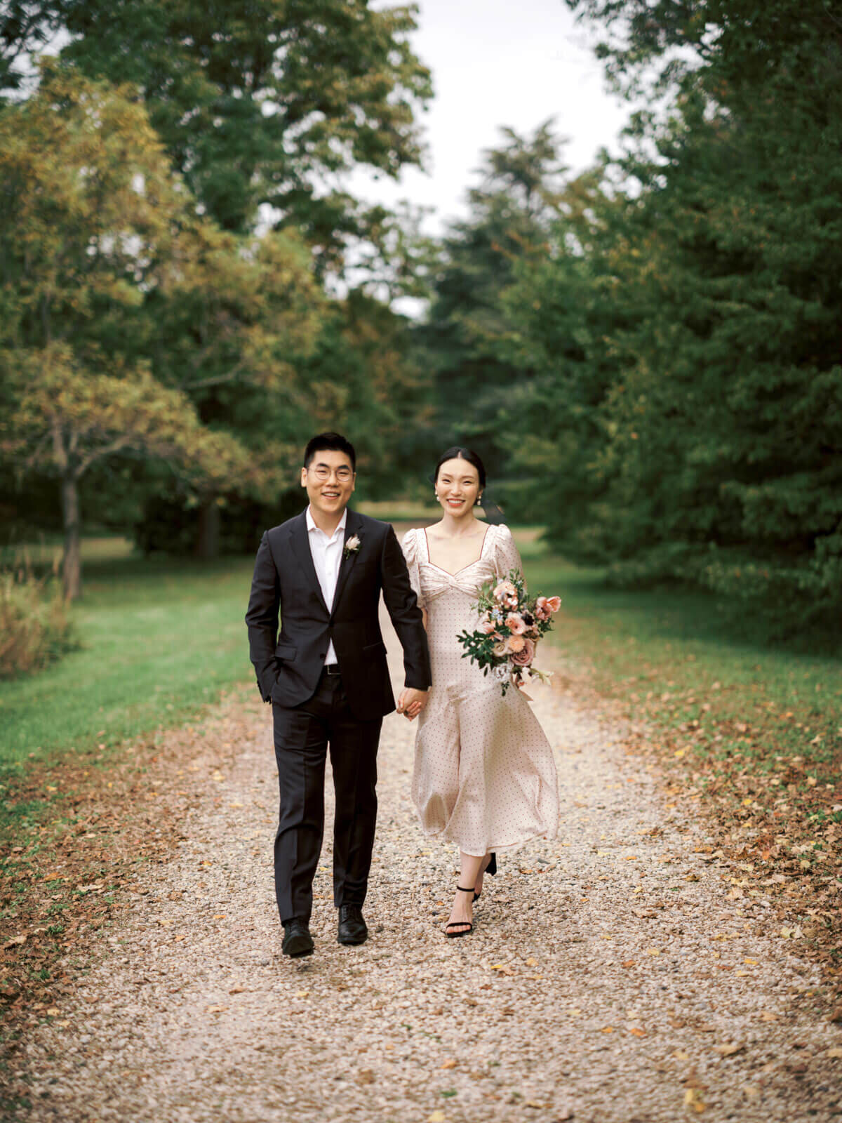 The engaged couple is walking on a trail filled with fall leaves, amidst the beautiful fall foliage. Image by Jenny Fu Studio