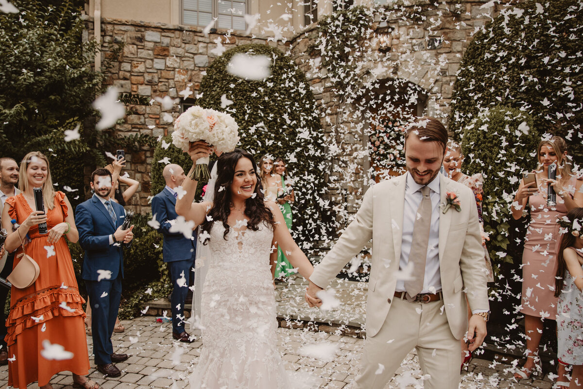 Newlyweds holding hands and walking as flower petals flow over them 
