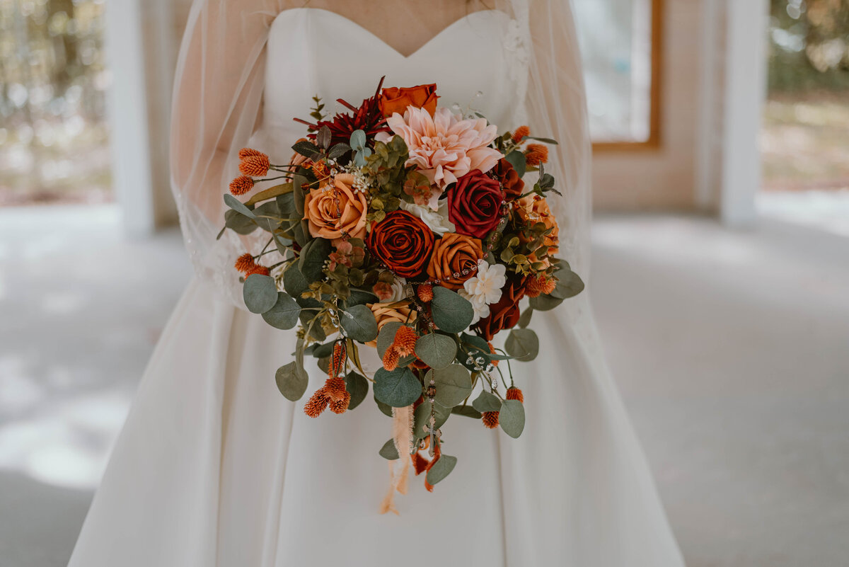 a wedding bouquet that consists of red, pink, and peach roses with green eucalyptus.