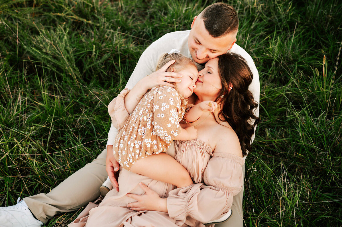 family cuddling holding pregnant baby bump in a field in Joplin MO during matenrity photography session