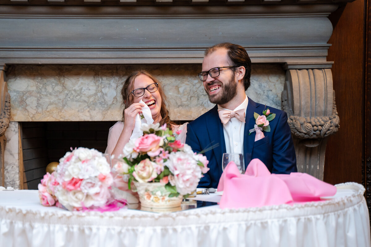 Groom laughs as he looks at his bride who's laughing and wiping away her tears during toasts at their wedding at the Akron Woman's City Club in Akron, Ohio.