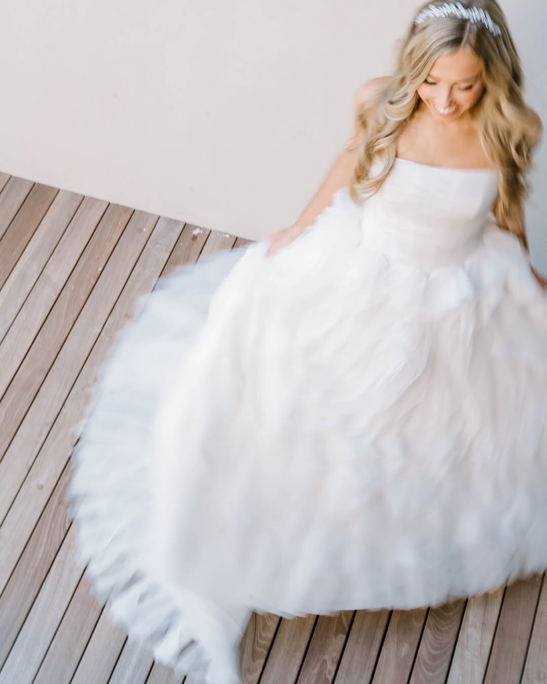 Wedding Photographer RI | Blurred image of a smiling woman in a flowing white wedding dress, twirling on a wooden deck. Her long blonde hair cascades over her shoulders.