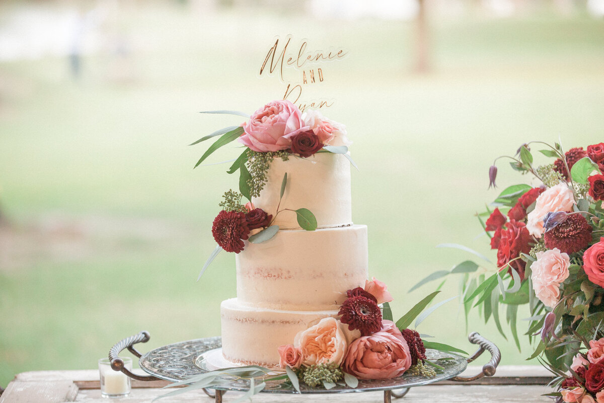 A three tiered cake decorated with white frosting and topped with roses, carnations, and eucalyptus