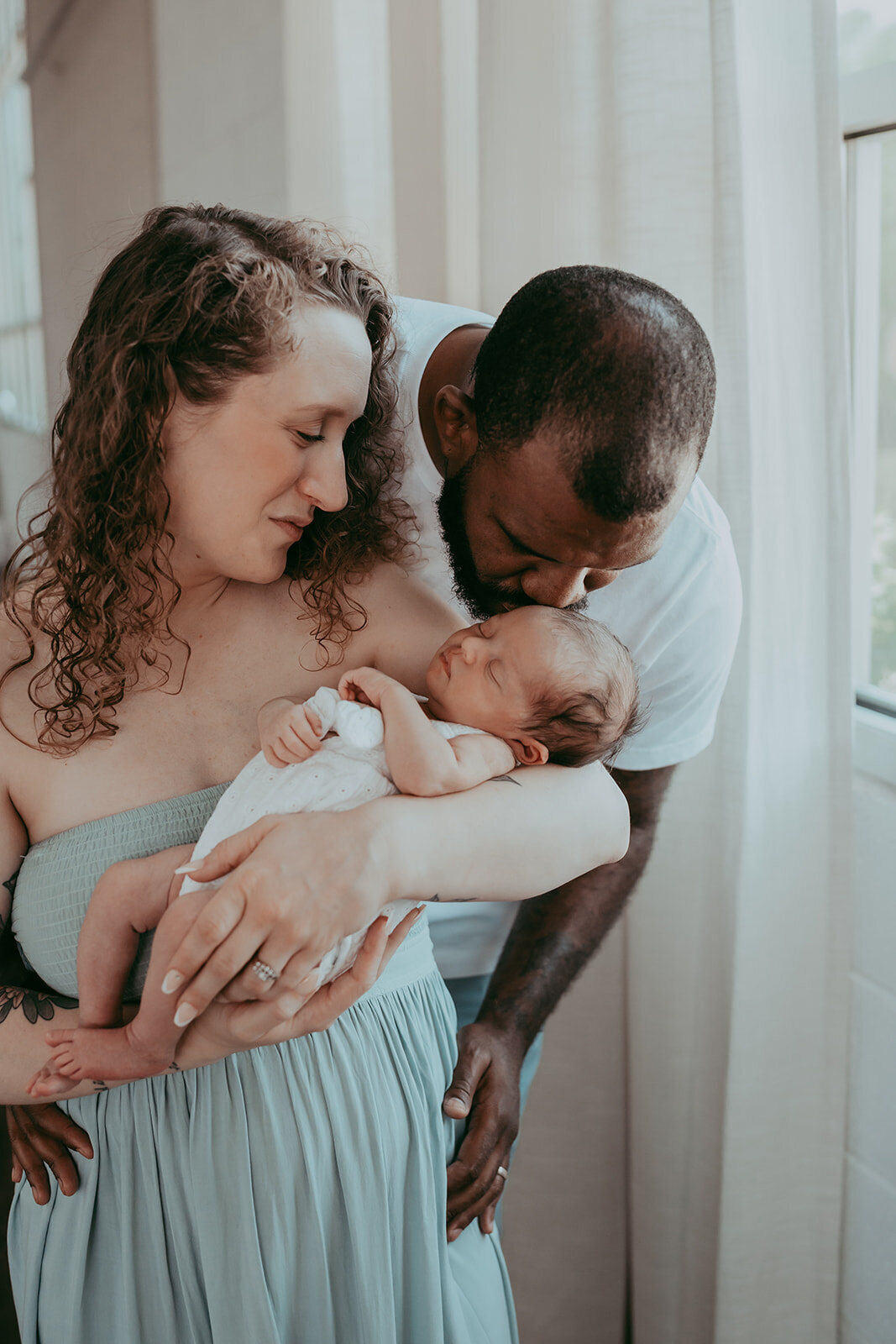 dad kisses his daughter as she is held by mom