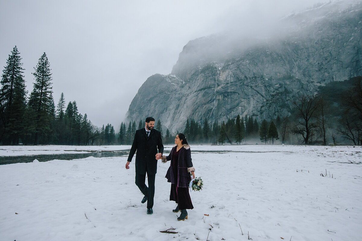 The bride and groom walk together in the snow in Yosemite