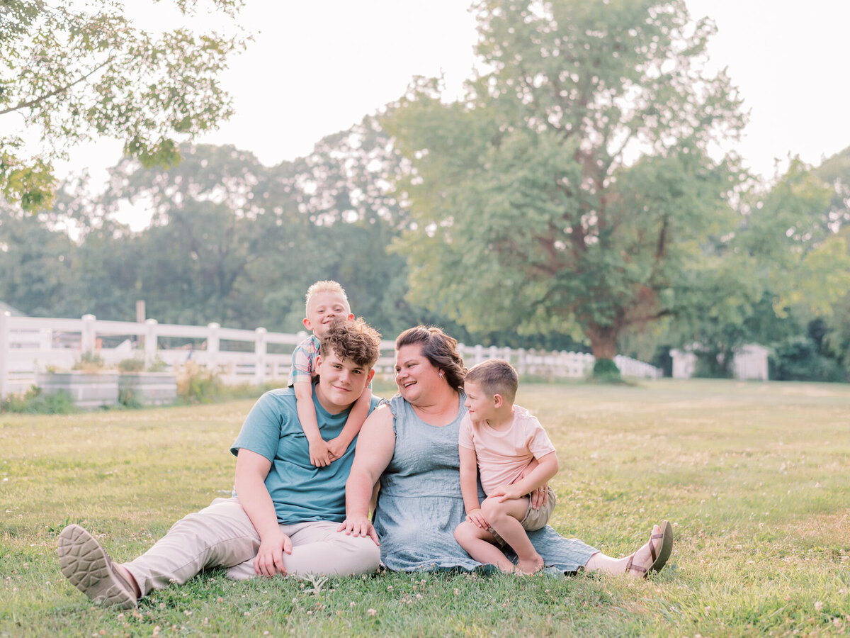 Mom and her three boys sitting in grass at park.