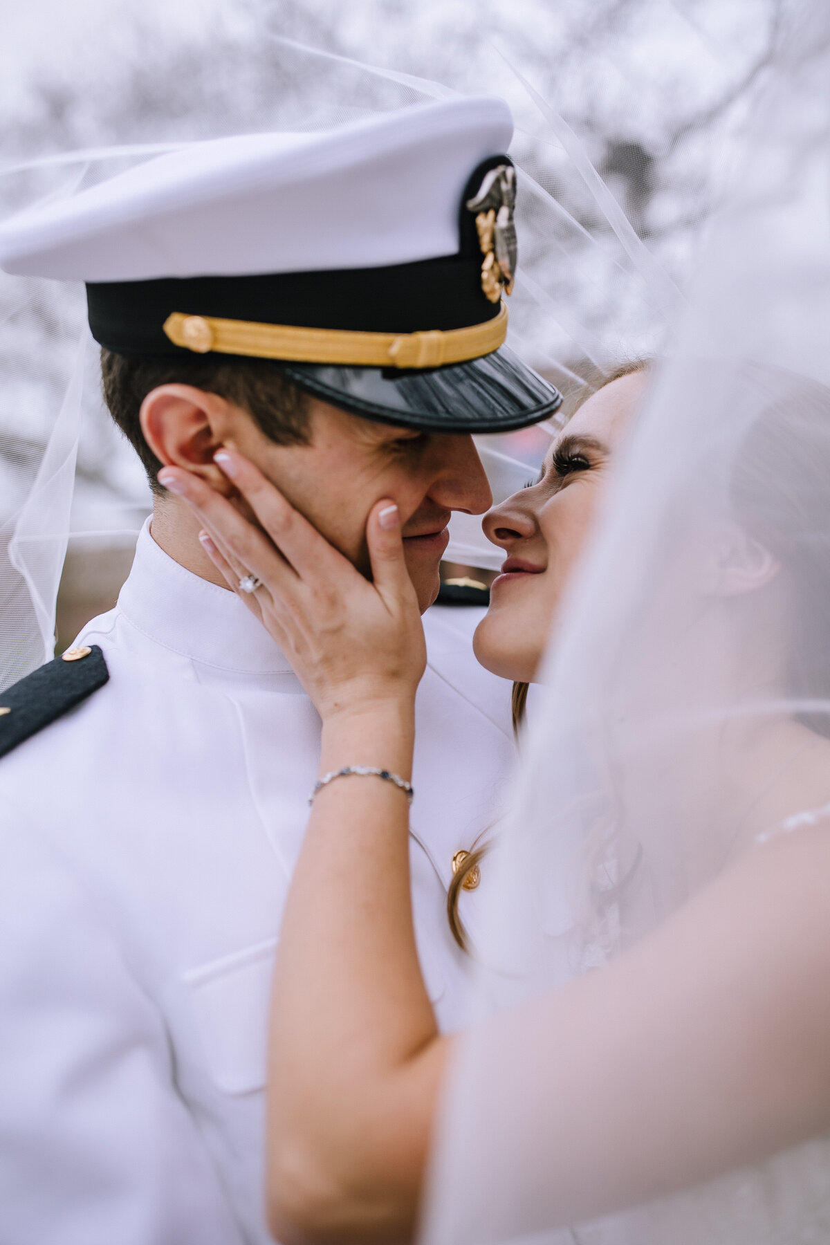 Military bride and groom kissing under a veil. 