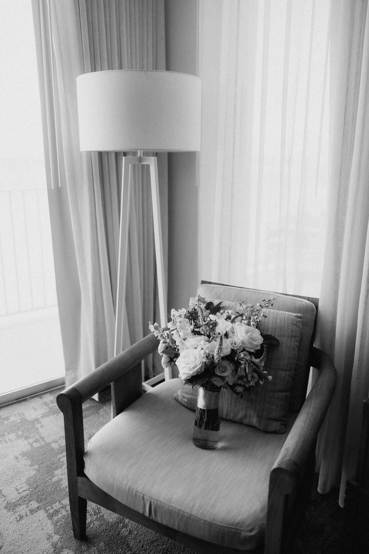 Bridal bouquet sitting on a chair with a lamp in the background and surrounded by beige curtains in black and white