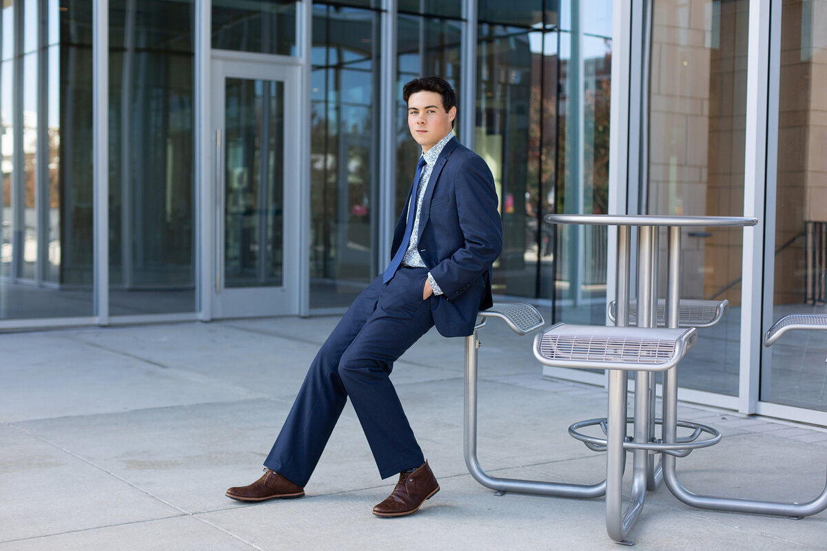 Peyton sitting in front of a glass wall with a blue suit in Downtown Birmingham for his senior pictures.