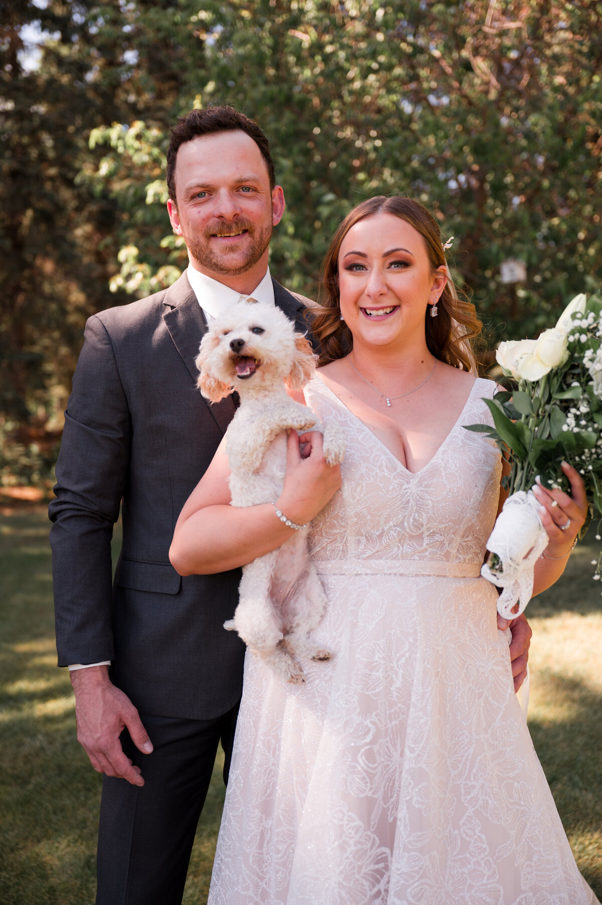 wedding couple holding their puppy smiling at the camera during wedding portrait