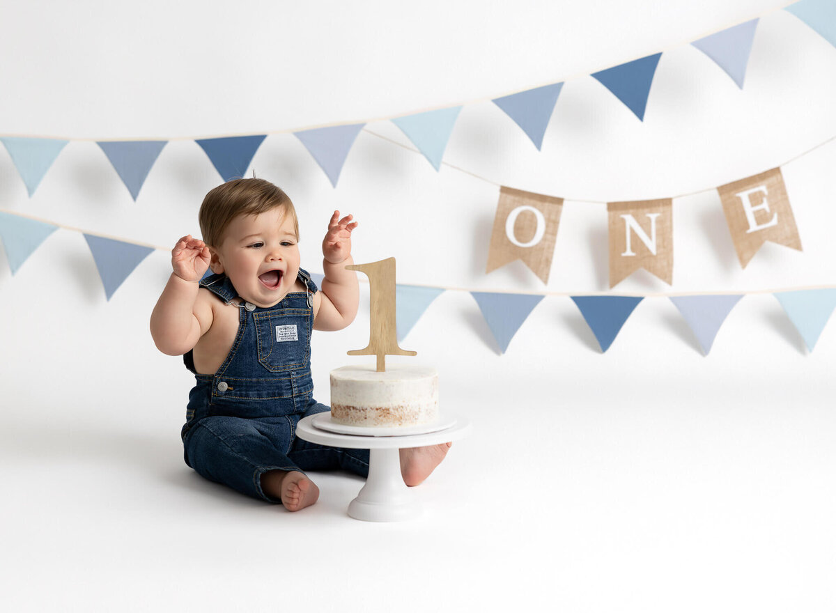 Boy in blue jean overalls and simple blue decorations for cake smash photographed by LV Photo Haus