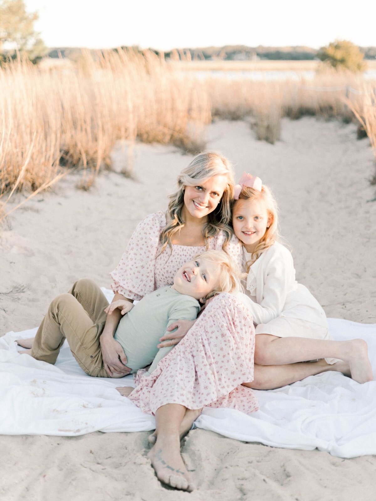 Mother sits on beach blanket smiling with two children Richmond Family Photography session.
