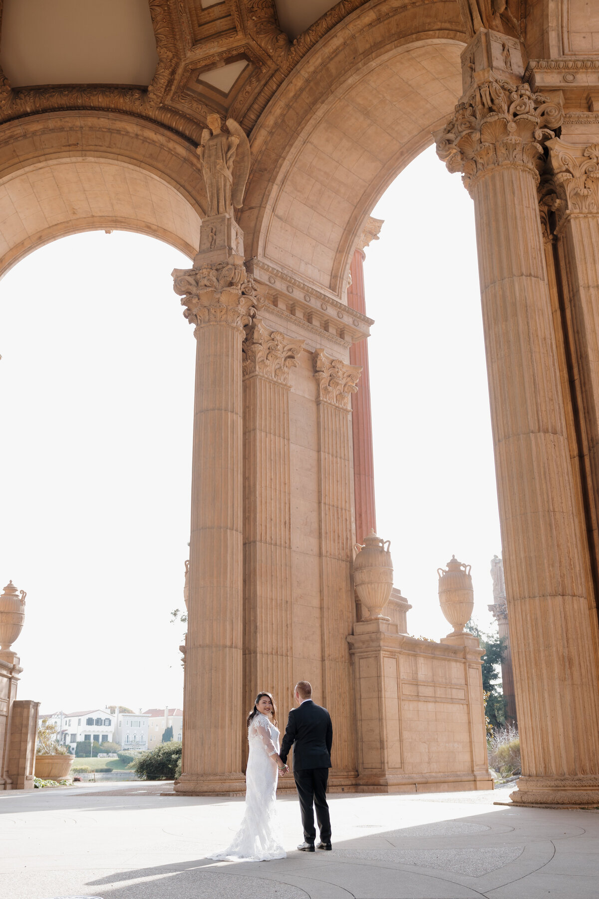 Bride and groom holding hands under grand architecture at Palace of Fine Arts, elegant San Francisco wedding photography.