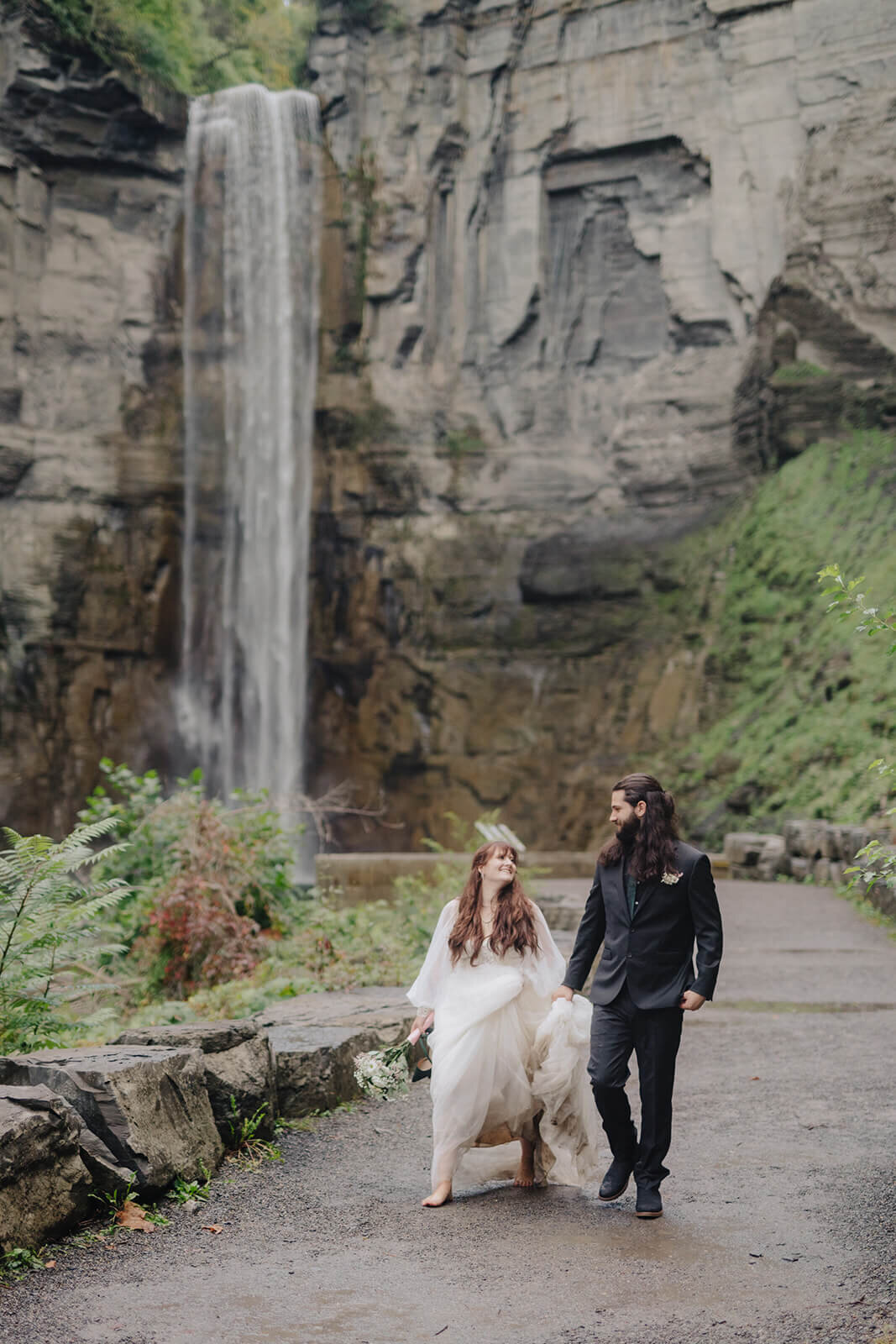 Bride and groom walking bare foot along path by a waterfall