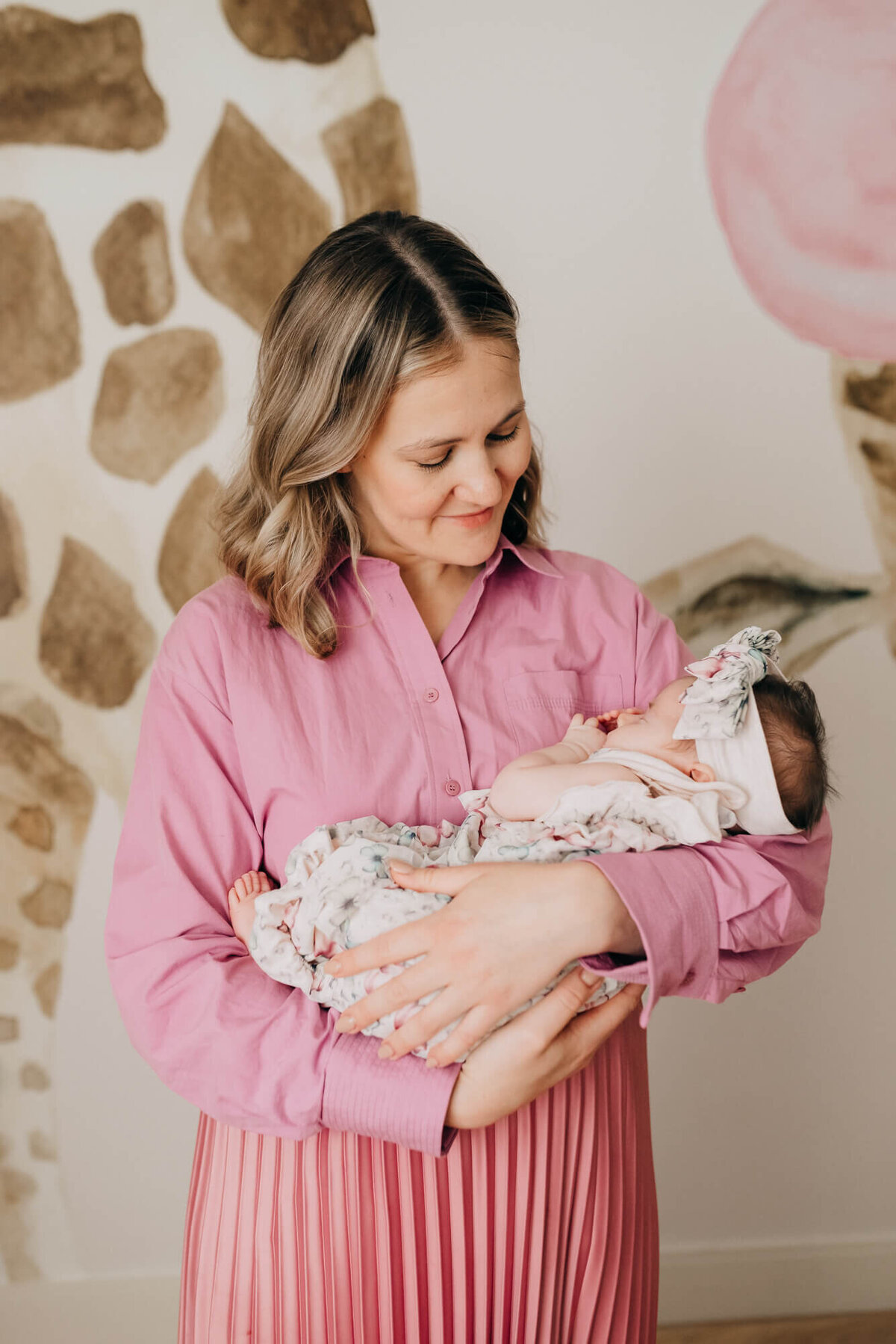 A mother wearing a soft pink outfit holds her daughter in her nursery
