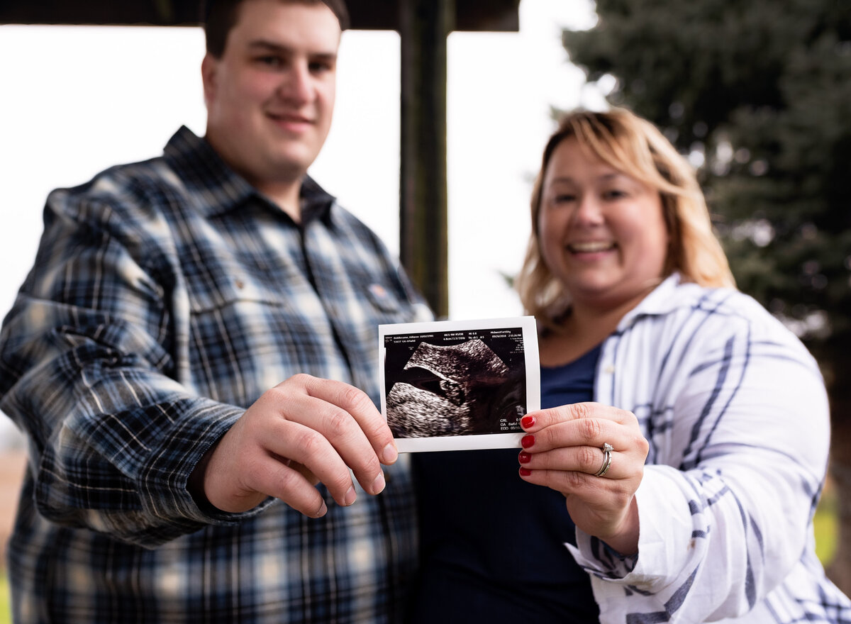 A joyful couple proudly holds an ultrasound photo, announcing their upcoming baby with bright smiles and excitement.
