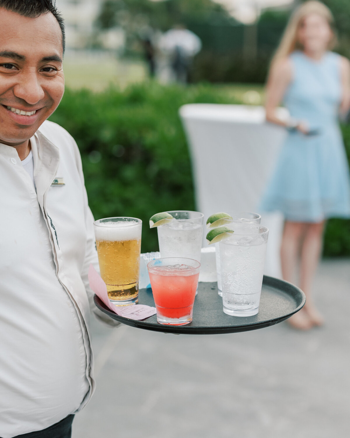 Cancun server smiling with cocktails on a tray, a joyful wedding reception moment by a Philadelphia destination photographer.
