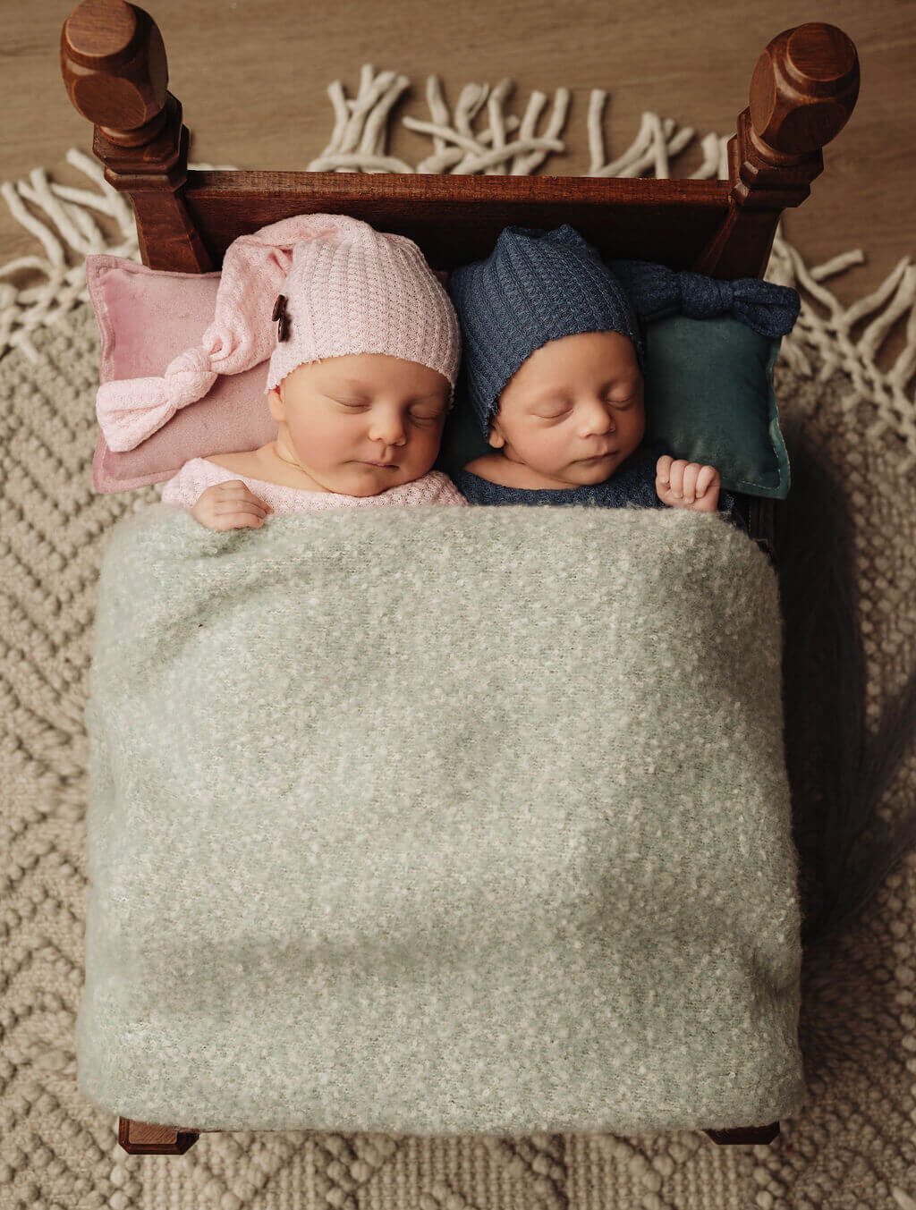 Newborn twins dressed in matching outfits sleeping in a studio bed prop at their newborn photo shoot in the Toronto area.