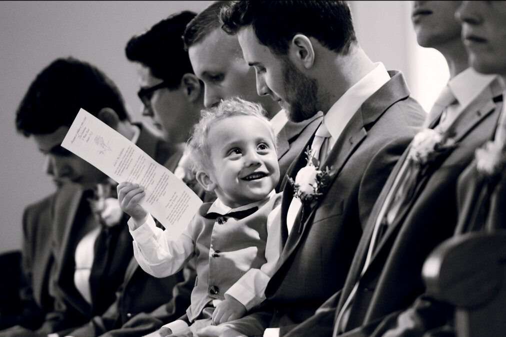 A little boy is reading a paper during a wedding ceremony.