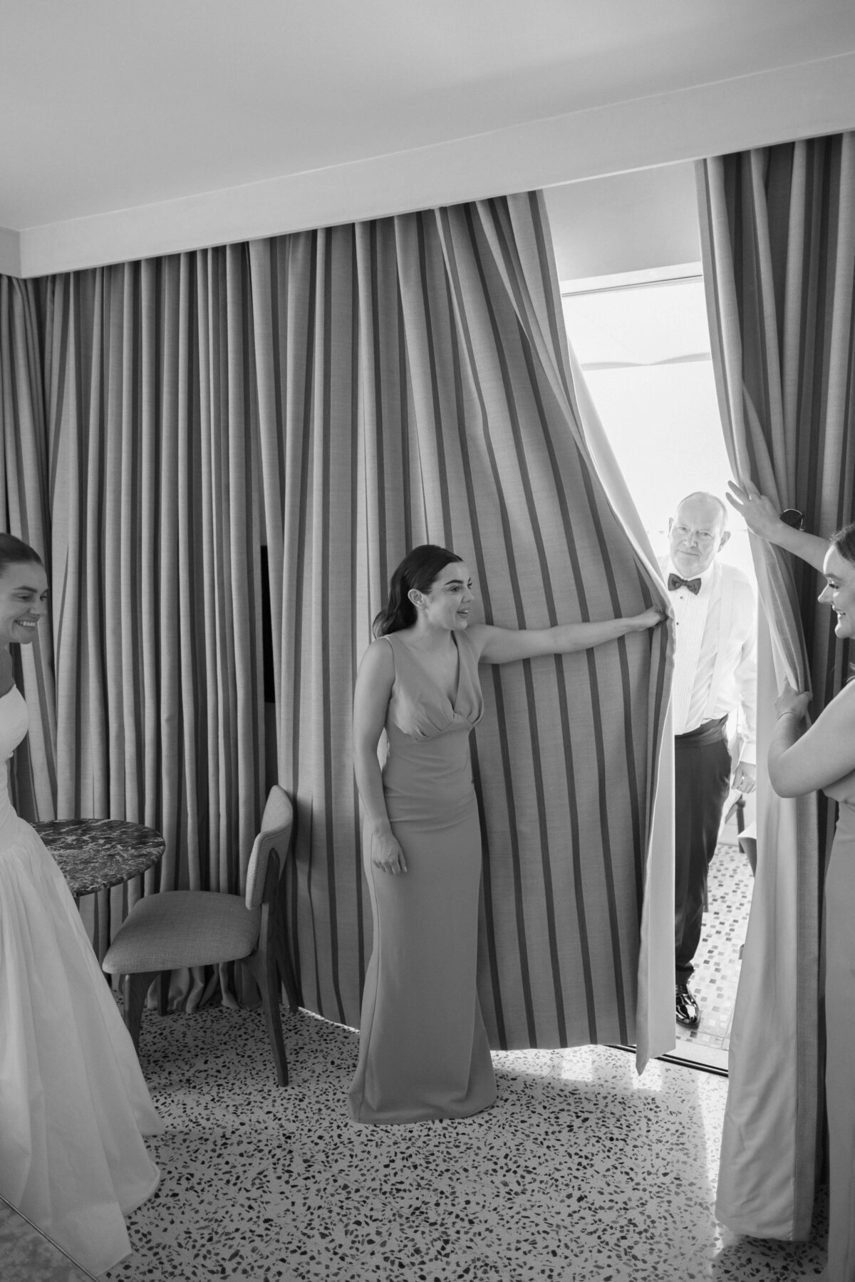 Bridesmaids assisting bride with gown in bright Rome hotel room

